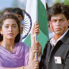 Ein "PRESS"-Ausweis an einem Jackett. Zwei Menschen halten eine indische Flagge, schauen ernst, im Hintergrund eine Menschenmenge.