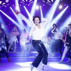 Ein fröhlicher Mann tanzt in einem Club. Umgeben von Leuten, bunte Lichter und dynamische Stimmung.