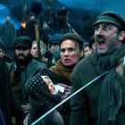 In der Szene stehen aufgebrachte Menschen in dicker Kleidung, einer schreit laut, eine Frau hält ein Kleinkind im Arm.