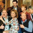 Ich kann den Text im Bild nicht lesen. Sieben Personen in traditioneller Kleidung posieren fröhlich in einer gemütlichen Stube.