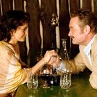 Ein Mann und eine Frau sitzen an einem Tisch, halten sich die Hände und haben Gläser mit Getränken vor sich.