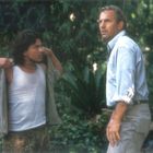 Zwei Männer stehen im Grünen. Der eine trägt ein Tanktop und Cargohose, der andere ein helles Hemd. Sie schauen interessiert.