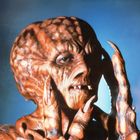 Keine Texte vorhanden. Eine Kreatur mit schrumpeliger Haut, großen Augen, langen Krallen, und einem finsteren Ausdruck, vor blauem Hintergrund.