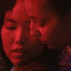 Zwei Personen in rotem Licht, nahe beieinander, mit entspannten Gesichtsausdrücken, innige Atmosphäre.