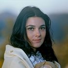 Keine Texte sichtbar. Eine Frau mit dunklen Haaren in Nahaufnahme, lächelnd, vor einem unscharfen Hintergrund.