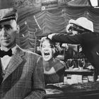 Der Text "Bürgerbräu aus Reichenhall" erscheint auf einem Schild. Eine lachende Frau, ein Mann in kariertem Anzug, Bar-Szene.