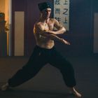 Chinesische Schriftzeichen auf einem Banner. Ein muskulöser Mann in Kampfpose in einem Raum mit asiatischer Dekoration.
