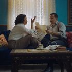 Ein Mann und eine Frau sitzen auf einem Sofa, diskutieren ein Dokument in einem stilvoll eingerichteten Wohnzimmer.