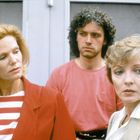 Drei Personen schauen ernst. Links eine Frau in rotem Blazer und gestreiftem Shirt, rechts eine Frau mit hellem Blazer.