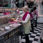 Eine Frau bereitet in einer weihnachtlich dekorierten Industrieküche Dessertteller vor. Lichterketten schmücken den Raum.