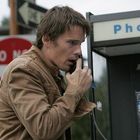 Ein Mann mit brauner Jacke telefoniert in einer Telefonzelle. Im Hintergrund ein "Do Not Enter"-Schild.