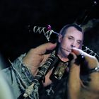 Es gibt keinen Text. Eine Hand hält eine kleine Holzpuppe mit einem darauf montierten Gesichtsfoto, durchbohrt von Nadeln.