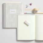 "NOTEBOOK" auf einem stilvollen Notizbuch, mit Stift, Radiergummi und Büroklammern daneben.