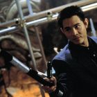 Ein Mann in einem Anzug hält eine Stange in der Hand, in einer Umgebung mit dekorativen Mustern im Hintergrund.