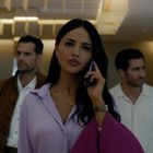 Eine Frau in lila Bluse telefoniert und wird von zwei Männern begleitet. Sie sind in einer modernen Lobby.