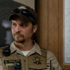 Name auf Uniform: G. TOOLEY. Ein Mann in Sheriff-Uniform mit Funkgerät und Karte im Hintergrund.