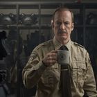 Ein Mann in einer Sheriff-Uniform hält eine Tasse mit einem Logo. Im Hintergrund sind Helme in einem Regal.