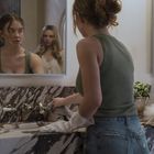 Zwei Frauen in einem Badezimmer, eine steht am Waschbecken, die andere ist im Spiegel zu sehen. Marmorausstattung, Pflanzen.