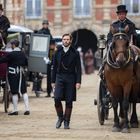 Keine sichtbaren Texte. Eine historische Szenerie mit Kutschen, Menschen in eleganter Kleidung und einem Pferd auf einem Platz.