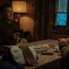 Eine Frau und ein Mann sitzen an einem Tisch mit einer bunten Decke. Vor ihnen liegen Geld, ein Taschenrechner und eine Tasche.