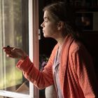 Keine Texte sichtbar. Eine Frau in einem orangefarbenen Bademantel hält eine Fliege am Fenster.