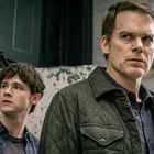 Zwei Männer stehen nachdenklich vor einer abgenutzten Wand. Einer trägt eine Jacke, der andere ein Hemd.