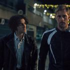 „Warehouse Clearance“ steht auf einem gelben Schild. Zwei Männer gehen abends unter Lichterketten.