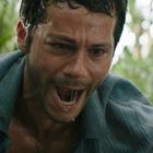 Ein Mann im blauen Hemd wirkt erschrocken und angespannt, umgeben von grüner Vegetation im Hintergrund.