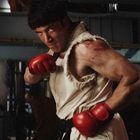 Ein muskulöser Mann mit roten Boxhandschuhen posiert in einem rauen, industriellen Umfeld und schaut entschlossen.