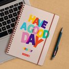 "Have a good day" steht bunt auf einem Spiralblock. Zusätzlich steht unten "2025/27" und "Brunnen". Ein Laptop und ein Stift sind sichtbar.