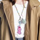 Beige Mantel, weiße Bluse, bunte Perlenkette mit Plüschanhänger und pinkem Hasenanhänger mit roter Schleife.