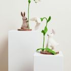 Zwei Filzhasen mit weißen Schneeglöckchen, jeweils auf weißen Sockeln präsentiert.