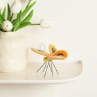 Weiße Tulpen in einer cremefarbenen Vase auf einem Regal; daneben ein dekorativer, bunter Filz-Schmetterling.