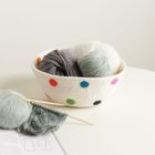 Keine sichtbaren Texte. Ein Korb mit bunten Punkten voller Garn. Ein Strickstück mit Nadeln liegt daneben.