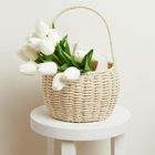 Ein geflochtener Korb mit weißen Tulpen und einer Toilettenpapierrolle auf einem weißen, runden Tisch.