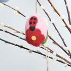 Ein Filzei mit roter Blume hängt an blühenden Zweigen. Im Hintergrund ein weiteres blaues Ei.