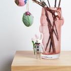 Ein heller Raum mit einer rosa Vase, Zweigen, Filzeiern und einer kleinen Filzhasenfigur.
