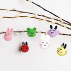 Sechs bunte, lächelnde Filztiere hängen an Zweigen: rosa Hase, grüner Frosch, lila Tier, rotes und gelbes Wesen, weißer Hase.