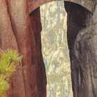 Kalender: April. Eine steinerne Brücke verbindet zwei massive Felsen über einer tiefen Schlucht. Darunter Berge in der Ferne.