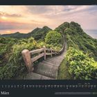 Text: „März“, Kalenderdaten. Eine steinerne Treppe schlängelt sich durch üppige grüne Hügellandschaft bei Sonnenuntergang.