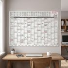 An der Wand hängt ein großer Jahreskalender für 2027 über einem Schreibtisch mit Laptop, Tasse und Pflanze.