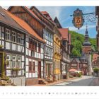 Das Bild zeigt eine malerische Altstadtstraße mit Fachwerkhäusern und einem Kirchturm im Hintergrund, darunter steht "4 · 2027".