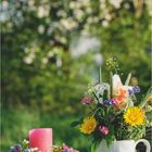 Landlust; März; Text: Willkommen im Frühling. Blühende Kränze und Sträuße auf Tisch im Garten, verschwommener blühender Hintergrund.