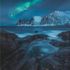 2 · 2027. Eine Landschaft mit Bergen, Meer, Felsen und grünen Polarlichtern am Himmel.