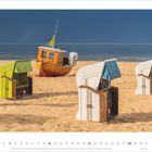 3-2027. Strandkörbe am Sandstrand, im Hintergrund ein Boot und das Meer unter einem dunklen Himmel.