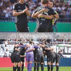 "Vorjahresabbildung" steht mittig in einem grauen Balken. Fußballspieler umarmen sich und bilden einen Kreis auf dem Spielfeld.