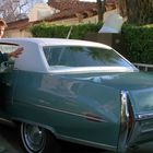 Nummernschild: "GRANDPA". Zwei Personen stehen neben einem hellblauen, klassischen Auto in einer Auffahrt.