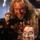 Der Text "Mutant Emporium" ist auf einer Figur. Eine Person mit hellem langen Haar und Bart lächelt hinter Figuren.