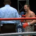 Der Text auf einem blauen Polster lautet "BA". Zwei Boxer im Ring, einer trägt Leoparden-Shorts, ein Schiedsrichter beobachtet.