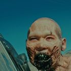 Unleserlicher Text links, kahle Figur mit vernarbter, monströser Fratze, weit geöffnetem Mund, Bäume und Himmel im Hintergrund.